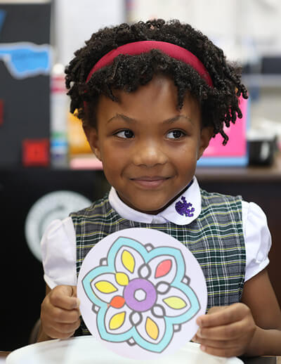 Preschool student holding a colourful paper craft in the classroom.