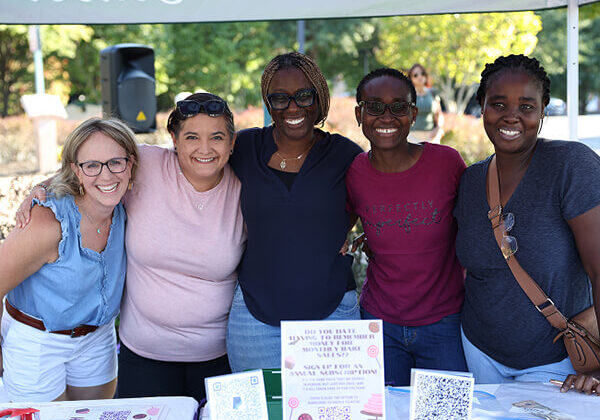 Group of smiling people standing together behind an information table at a school event.